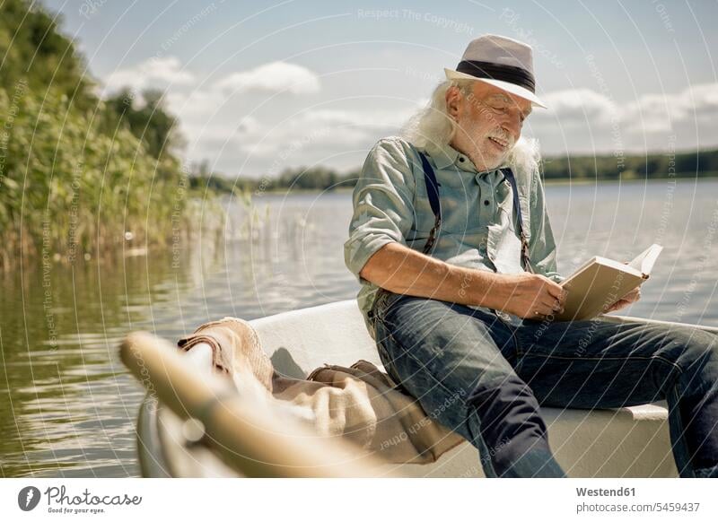 Portrait of content senior man sitting in rowing boat on a lake reading a book books portrait portraits senior men elder man elder men senior citizen pleased