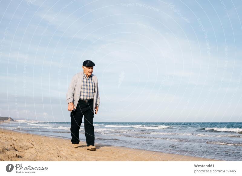 Senior man strolling on the beach in spring relaxation relaxing tranquility tranquillity Calmness age cap caps beach stroll walking along the beach