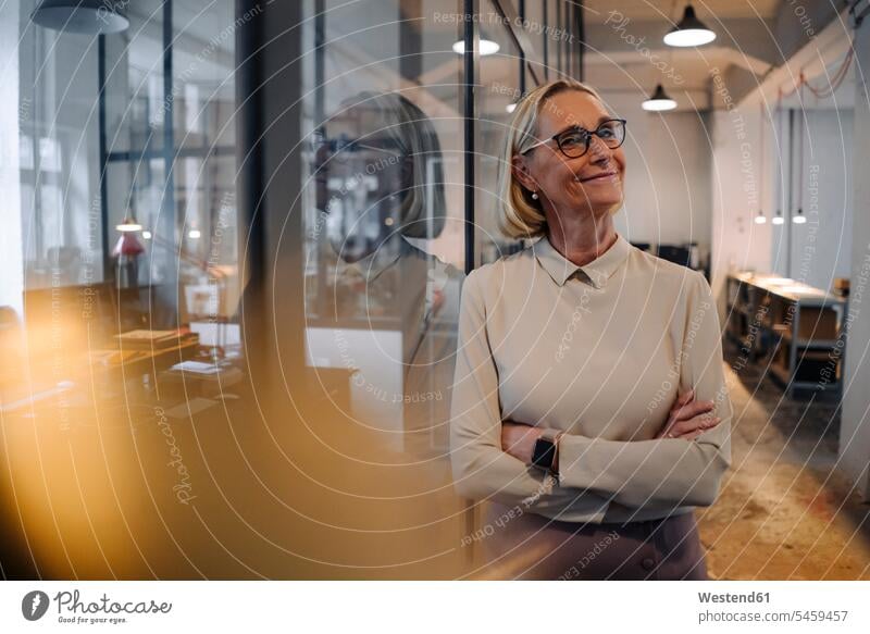 Portrait of smiling mature businesswoman leaning against glass pane in office Occupation Work job jobs profession professional occupation business life