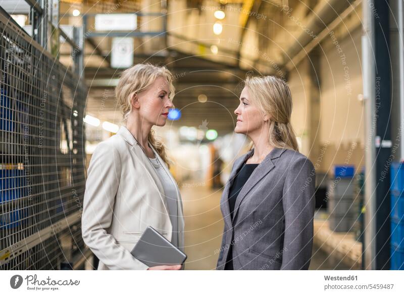Two women facing each other in factory storehouse storage warehouse looking eyeing woman females industrial hall shop floor factory hall industrial buildings