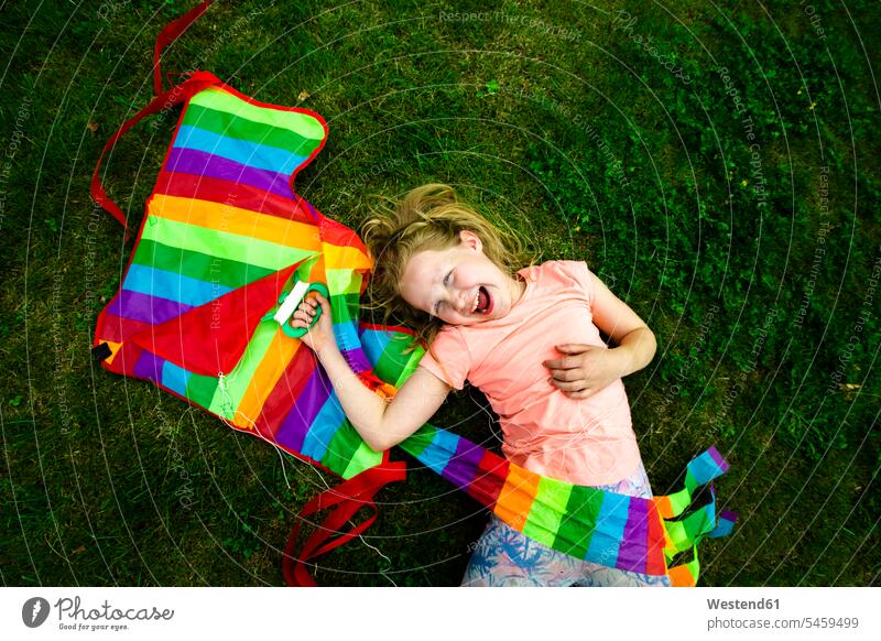 Happy girl holding colorful kite while lying down in park color image colour image outdoors location shots outdoor shot outdoor shots day daylight shot