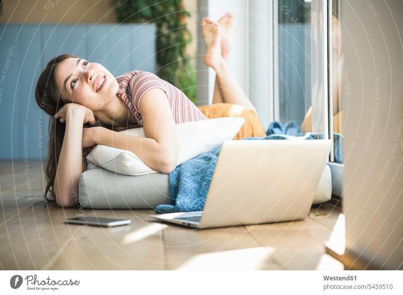Relaxed young woman lying at the window at home with laptop laying down lie lying down females women relaxed relaxation smiling smile Adults grown-ups grownups