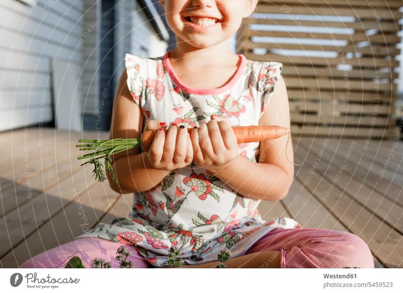 Little girl sitting on terrace holding carrot, partial view human human being human beings humans person persons caucasian appearance caucasian ethnicity