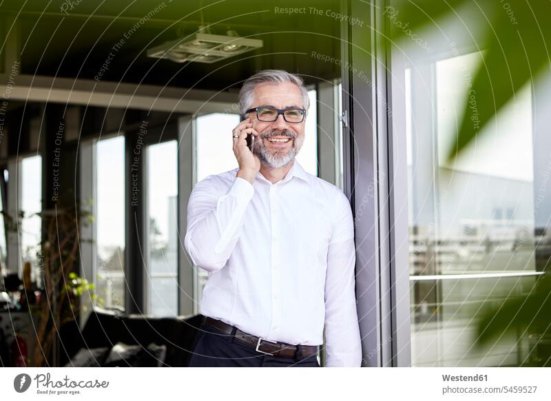 Smiling businessman standing at French door talking on cell phone on the phone call telephoning On The Telephone calling smiling smile French Door window