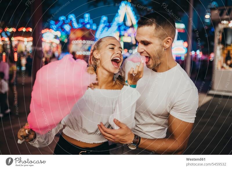 Cheerful young woman feeding cotton candy to boyfriend at amusement park color image colour image Spain leisure activity leisure activities free time