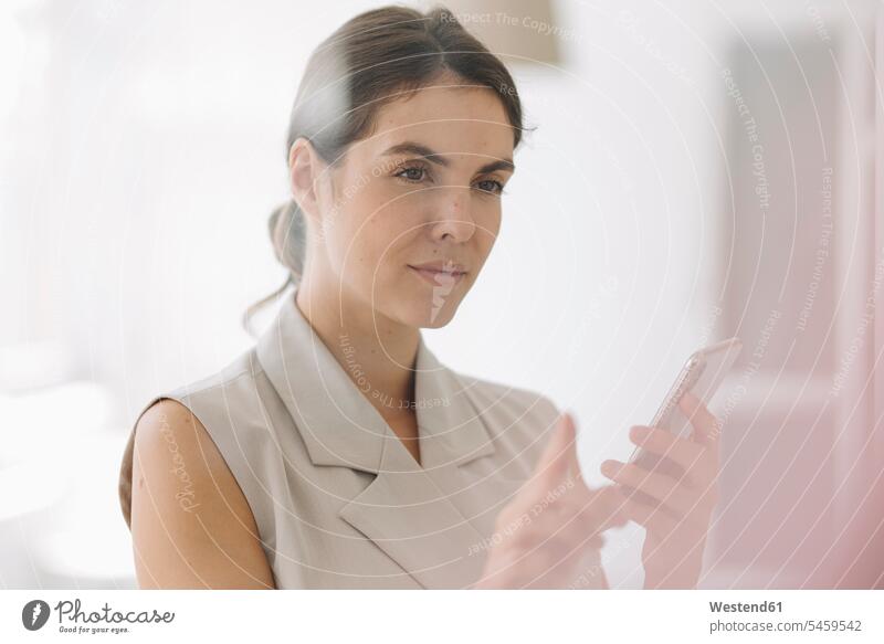 Woman pointing at glass wall while using mobile phone at office color image colour image indoors indoor shot indoor shots interior interior view Interiors day