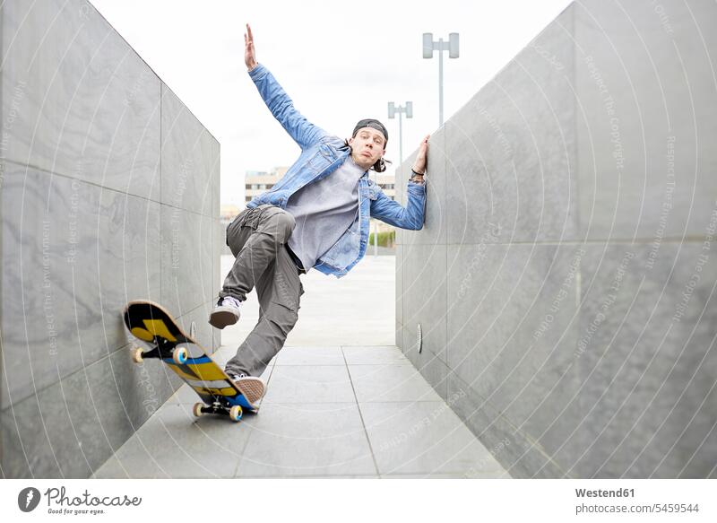 Young man skateboarding in the city balancing balance passage gateway young man young men wall walls cool attitude composed coolness laid-back Skate Board