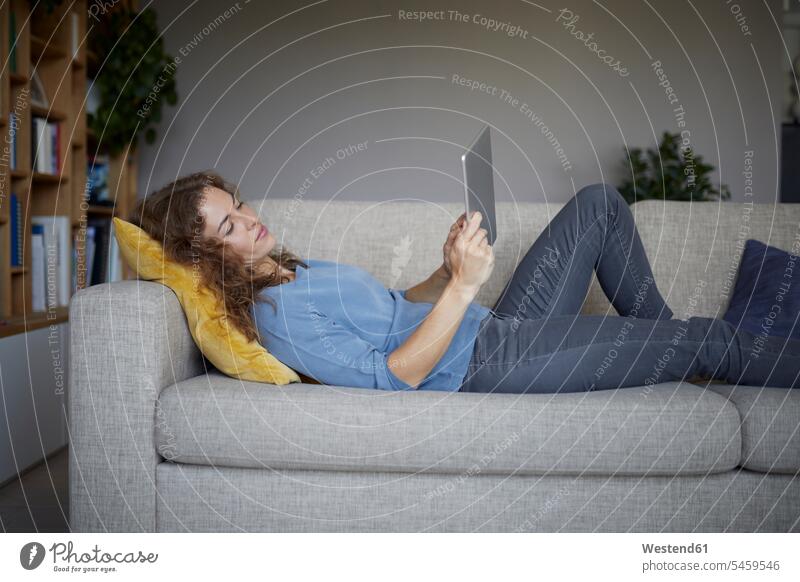 Woman using digital tablet while lying on sofa at home color image colour image indoors indoor shot indoor shots interior interior view Interiors day