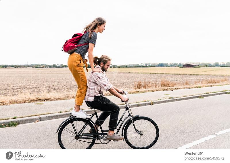 Happy young couple riding together on one bicycle on country road bikes bicycles happiness happy twosomes partnership couples rural road rural roads