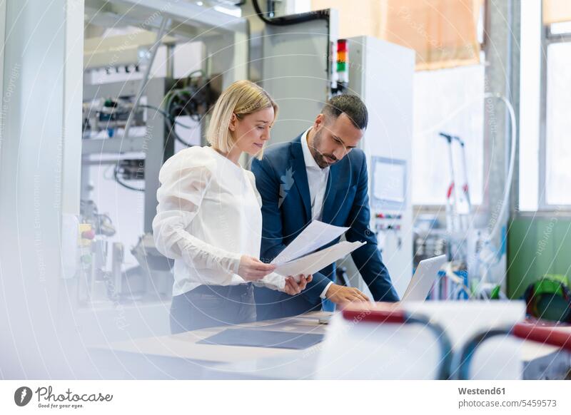 Businessman and young woman with papers and laptop talking in a factory Occupation Work job jobs profession professional occupation business life business world
