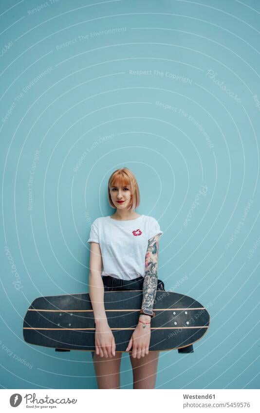 Portrait of cool young woman holding carver skateboard standing at turquoise wall portrait portraits cool attitude composed coolness laid-back Skate Board