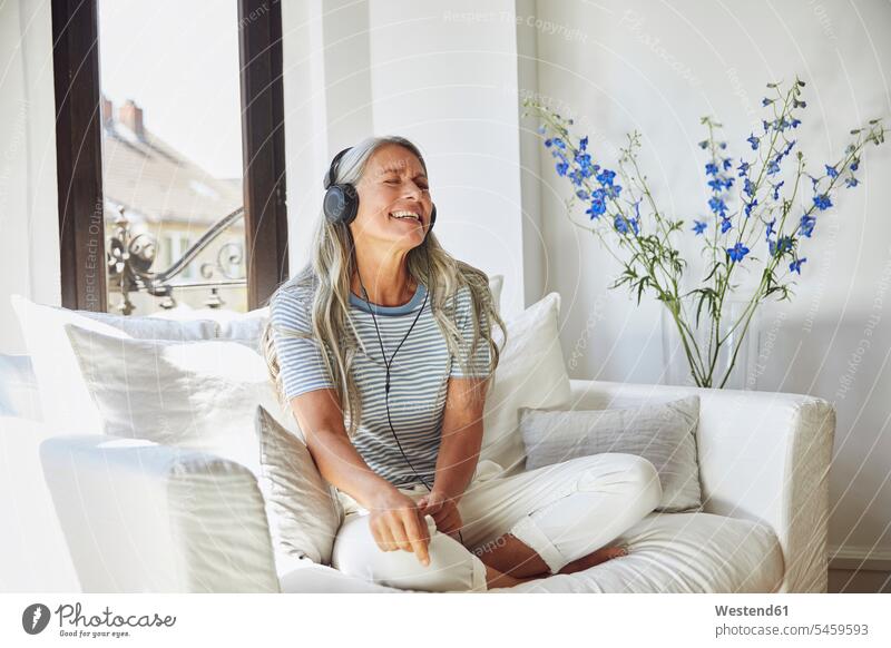 Happy woman listening to music through headphones on sofa at home Germany indoors indoor shot indoor shots interior interior view Interiors day daylight shot