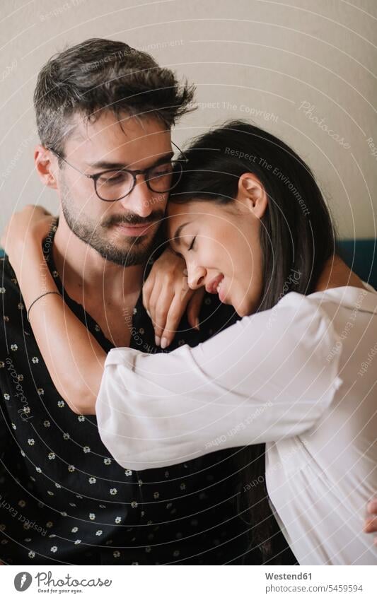 Young couple in love cuddling on a couch couches settee settees sofa sofas Eye Glasses Eyeglasses specs spectacles cuddle snuggle snuggling smile Seated sit
