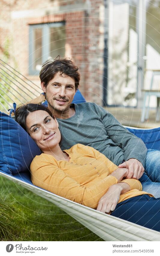 Smiling couple lying in hammock in garden of their home laying down lie lying down house houses smiling smile twosomes partnership couples hammocks gardens