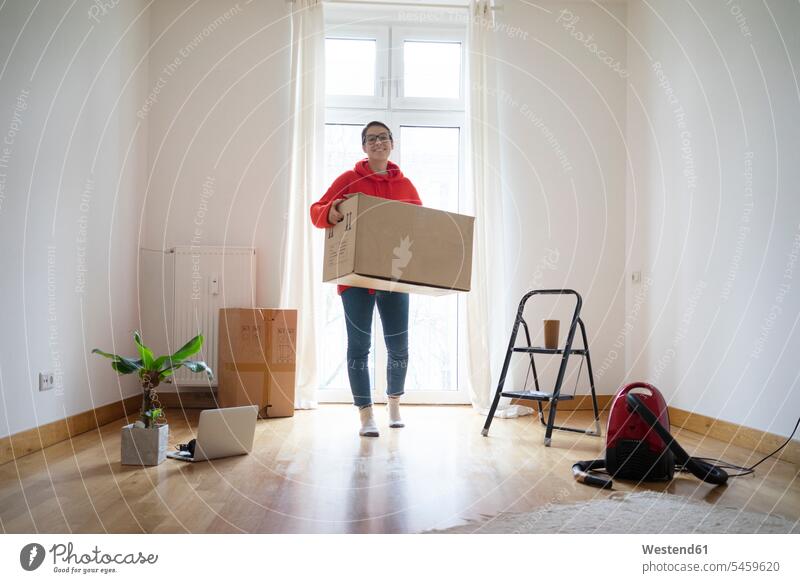 Young woman moving into her new home, carrying a cardboard box Foliage Plant Foliage Plants young women young woman cardboard boxes packing case packing cases