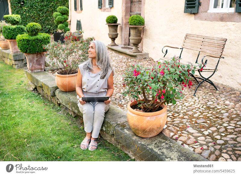 Woman with long grey hair sitting on terrace at country house using tablet woman females women Seated smiling smile country houses cottage cottages