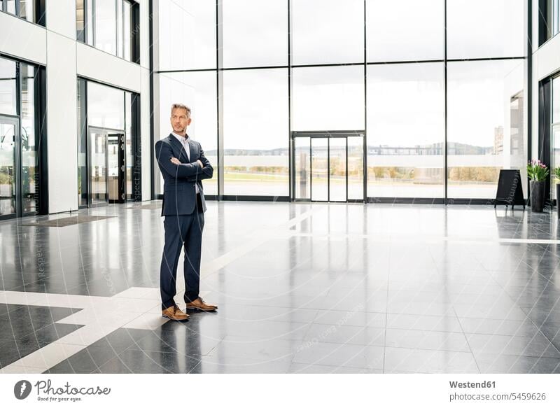 Successful businessman standing in entrance hall of office building, with arms crossed human human being human beings humans person persons caucasian appearance