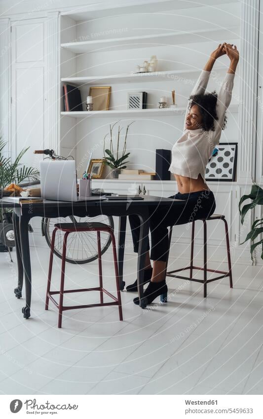 Mid adult woman sitting in her home office, smiling and stretching Seated freelancer freelancing working At Work working from home home business working at home