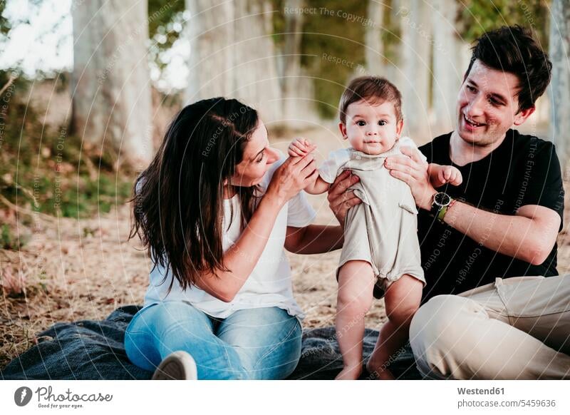 Smiling parents playing with baby boy while sitting on blanket outdoors color image colour image location shots outdoor shot outdoor shots day daylight shot
