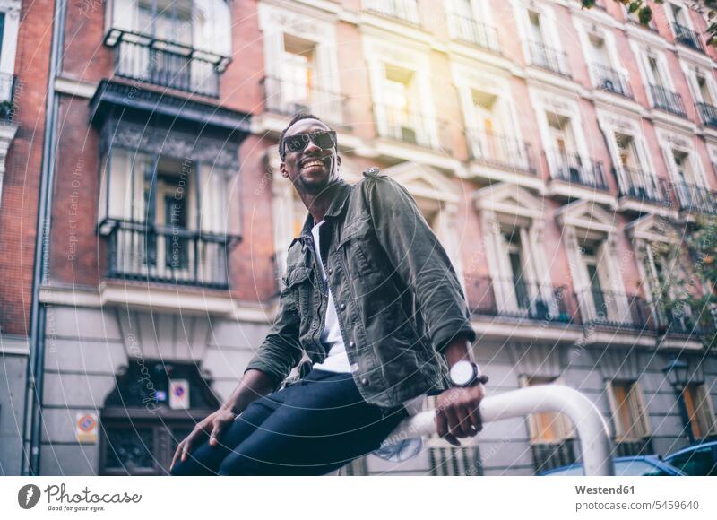 Smiling man wearing sunglasses sitting against building in city color image colour image Spain leisure activity leisure activities free time leisure time