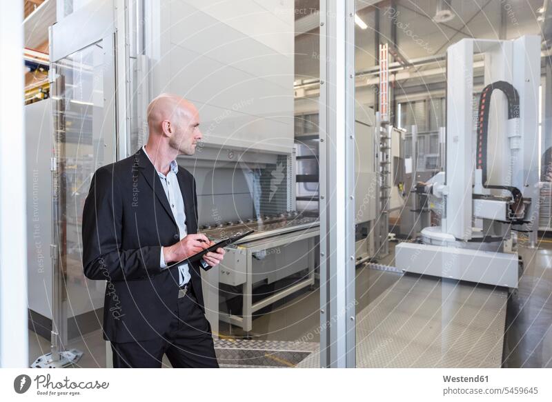 Businessman looking at machine in modern factory Business man Businessmen Business men contemporary factories eyeing device devices business people