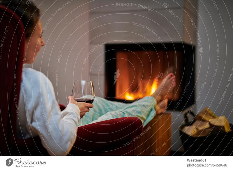 Woman sitting on armchair with glass of red wine relaxing in front of fireplace human human being human beings humans person persons adult grown-up grown-ups