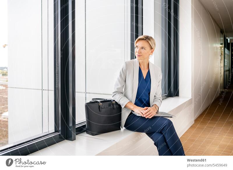 Blond businesswoman with laptop, sitting on windowsill in office building human human being human beings humans person persons caucasian appearance