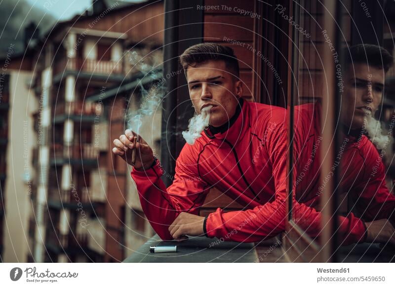 Young men smoking while looking out of window color image colour image outdoors location shots outdoor shot outdoor shots day daylight shot daylight shots