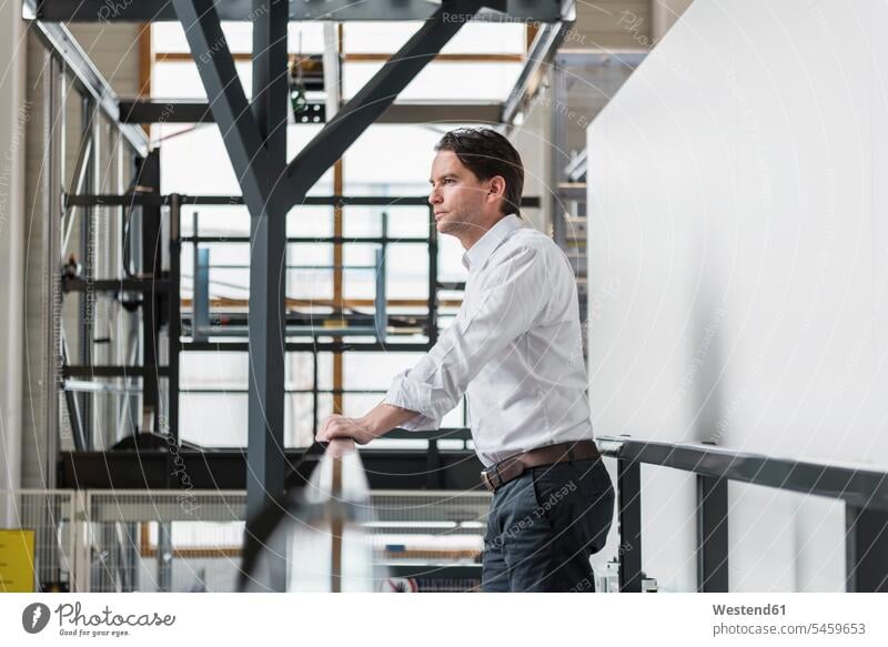 Businessman standing at railing in factory thinking factories Railing Railings Business man Businessmen Business men business people businesspeople
