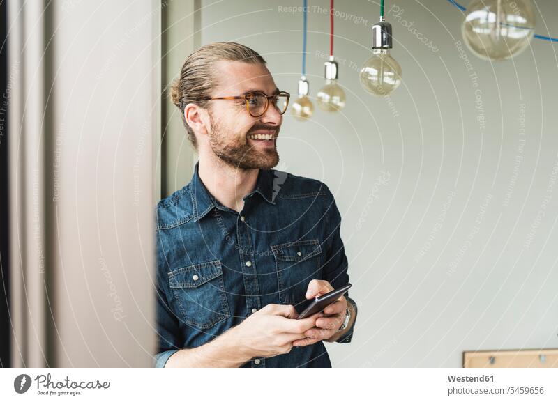 Smiling young businessman holding cell phone at the window in office mobile phone mobiles mobile phones Cellphone cell phones smiling smile offices office room