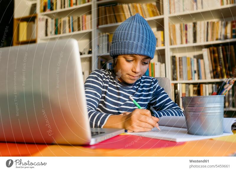 Smiling boy wearing knit hat writing in book while sitting at home color image colour image 10-11 years 10 to 11 years children kid kids people human being