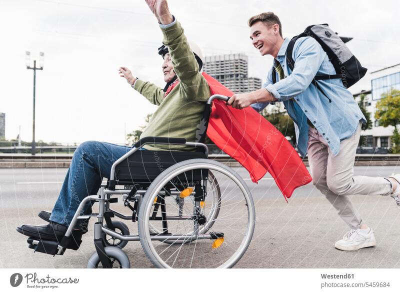 Young man pushing senior man sitting in a wheelchair dressed up as superhero human human being human beings humans person persons caucasian appearance