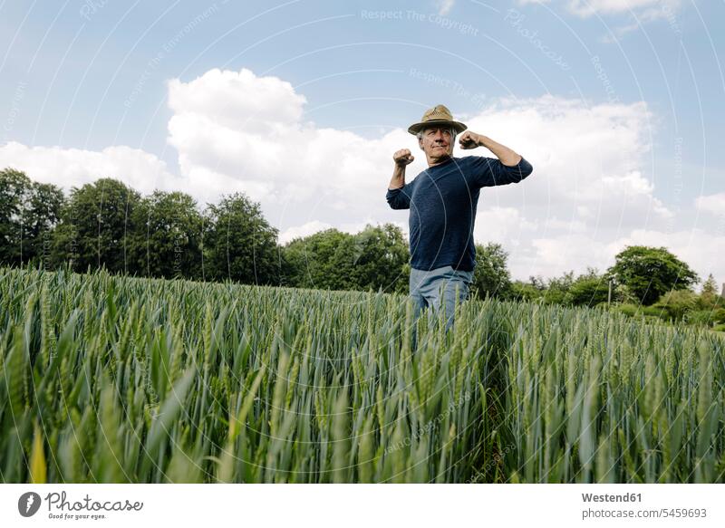 Confident man flexing muscles against cloudy sky in field color image colour image outdoors location shots outdoor shot outdoor shots day daylight shot