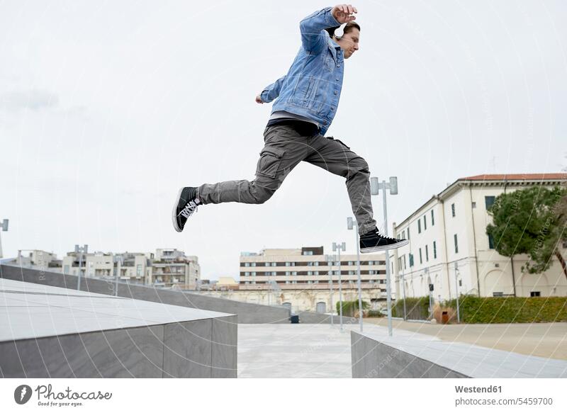 Young man jumping over gap between walls, mid air Listening Music cool attitude composed coolness laid-back young man young men mid-air midair Leaping males