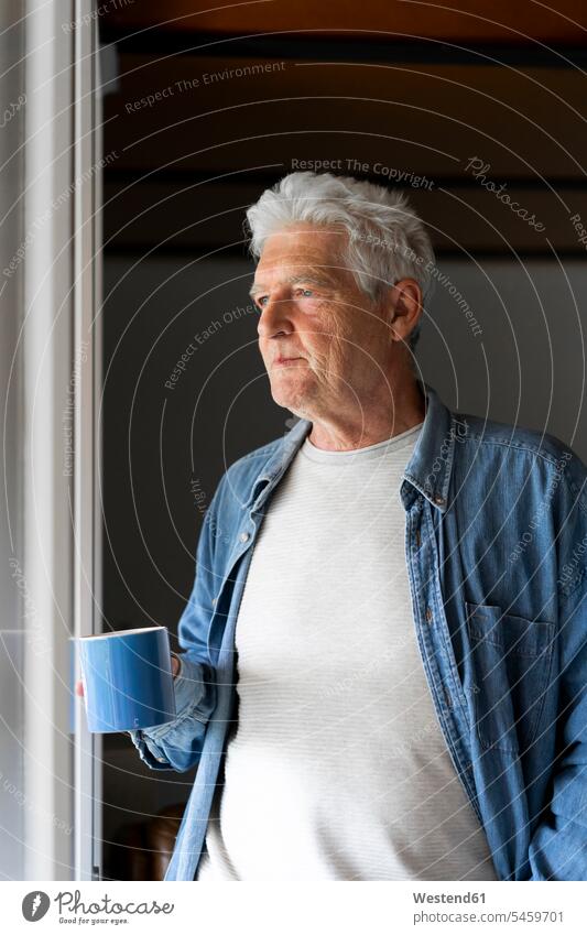Thoughtful senior man holding coffee mug while looking through window at home color image colour image indoors indoor shot indoor shots interior interior view