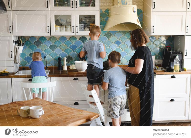 Mother cooking with her three sons in the kitchen Bowls T- Shirt t-shirts tee-shirt chairs stand at home domestic kitchen kitchens back view view from the back