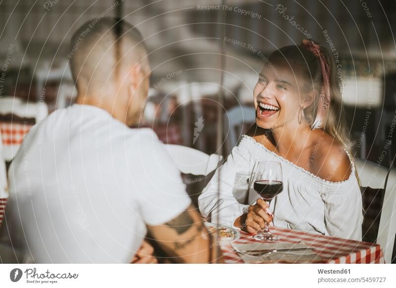Happy woman holding wineglass looking at boyfriend in restaurant seen through window 20-25 years 20 to 25 years young women young woman 25-30 years