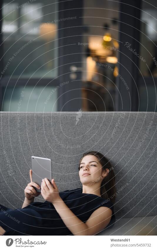 Portrait of young woman with digital tablet lying on couch looking at distance human human being human beings humans person persons caucasian appearance