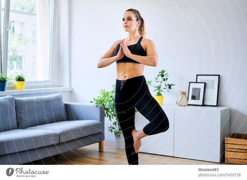 Woman in sports clothing practicing tree pose at home color image colour image indoors indoor shot indoor shots interior interior view Interiors Home Interior