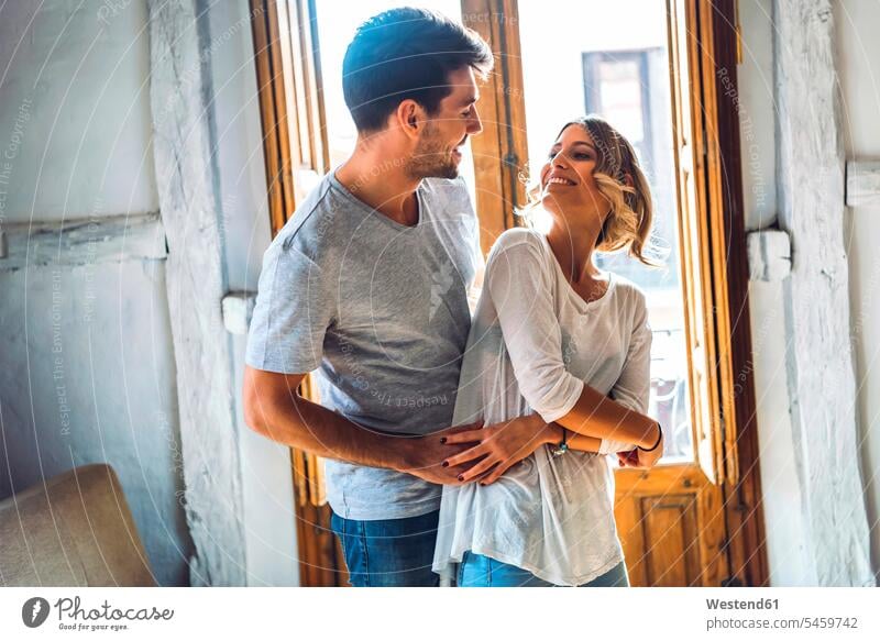 Affectionate young couple dancing in living room at home windows smile embrace Embracement hug hugging delight enjoyment Pleasant pleasure happy passionate