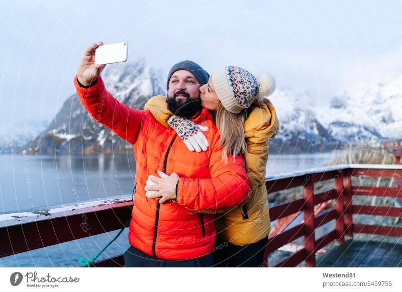 Tourist couple taking a selfie at Hamnoy, Lofoten, Norway touristic tourists coat coats jackets telecommunication phones telephone telephones cell phone