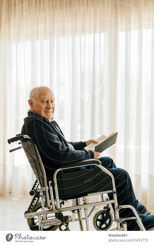 Portrait of smiling senior man sitting in wheelchair with a book human human being human beings humans person persons caucasian appearance caucasian ethnicity