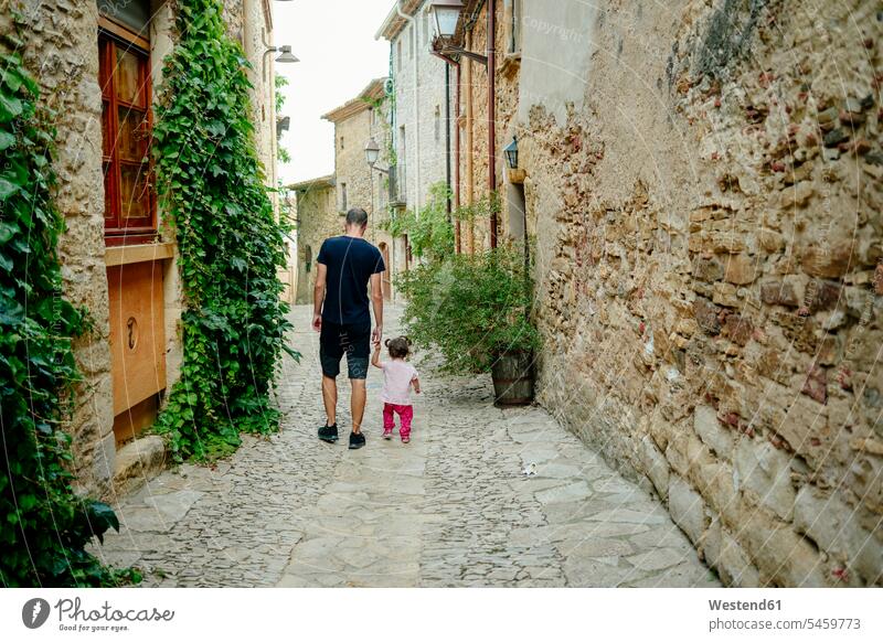 Spain, Catalonia, Peratallada, Medieval Town, Father and daughter walking hand in hand, rear view alley lane Laneway daughters going father fathers daddy dads