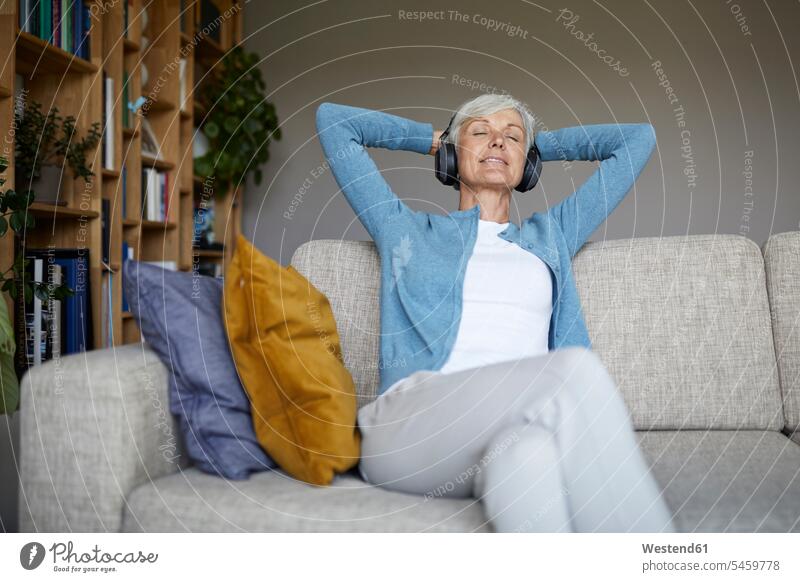 Woman with hands behind head listening to music through headphones at home color image colour image indoors indoor shot indoor shots interior interior view
