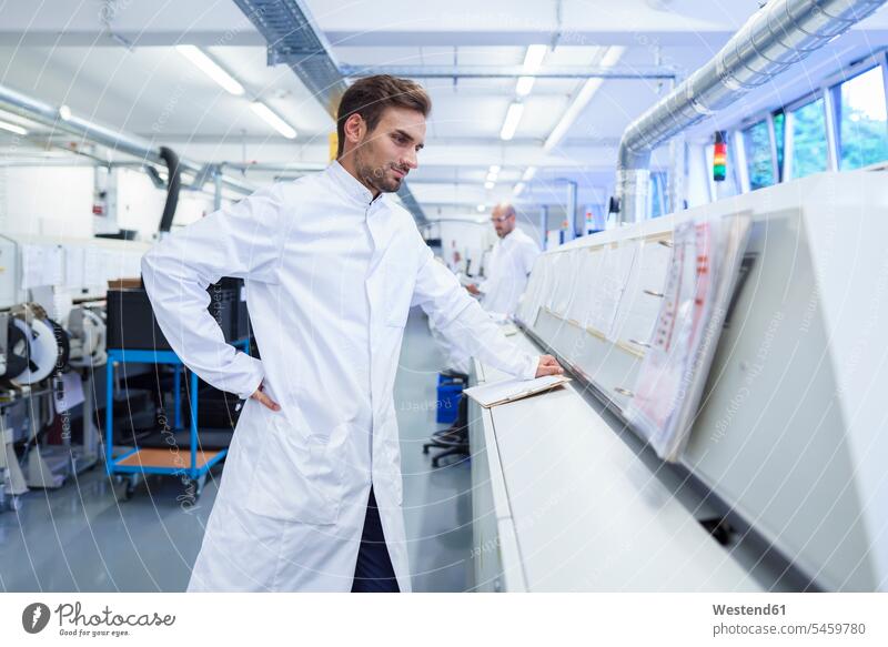 Young male technician in lab coat looking at reports on machinery color image colour image indoors indoor shot indoor shots interior interior view Interiors