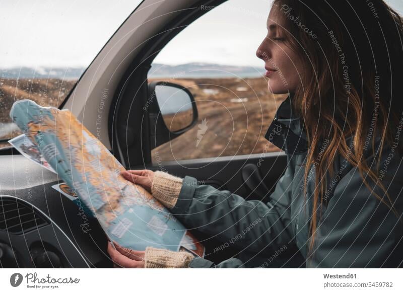 Iceland, young woman in car looking at map maps eyeing automobile Auto cars motorcars Automobiles females women view seeing viewing motor vehicle road vehicle
