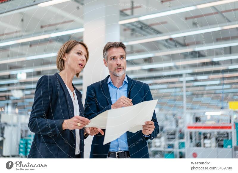 Businessman and businesswoman discussing plan in a factory hall business life business world business person businesspeople associate associates