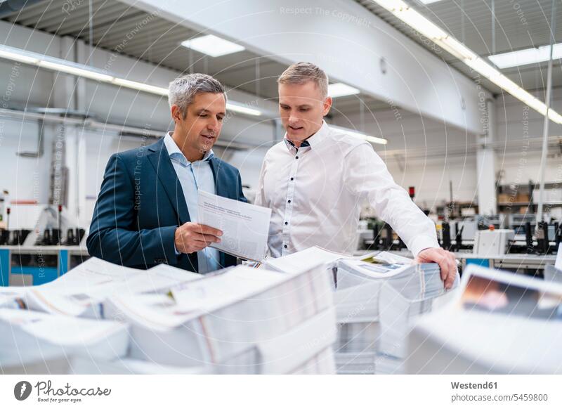 Two businessmen discussing paper in a factory business life business world business person businesspeople associate associates business associate