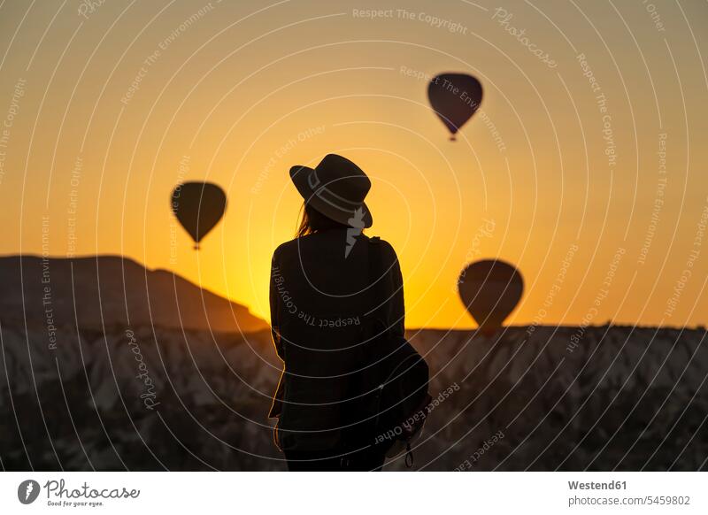 Rear view of silhouette young woman looking at hot air balloons while standing on land at Goreme, Cappadocia, Turkey Adventure Adventures adventurous