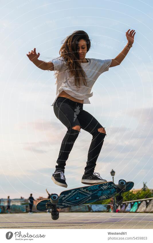 Young woman doing a skateboard trick in the city females women town cities towns Trick Skate Board skateboards Adults grown-ups grownups adult people persons